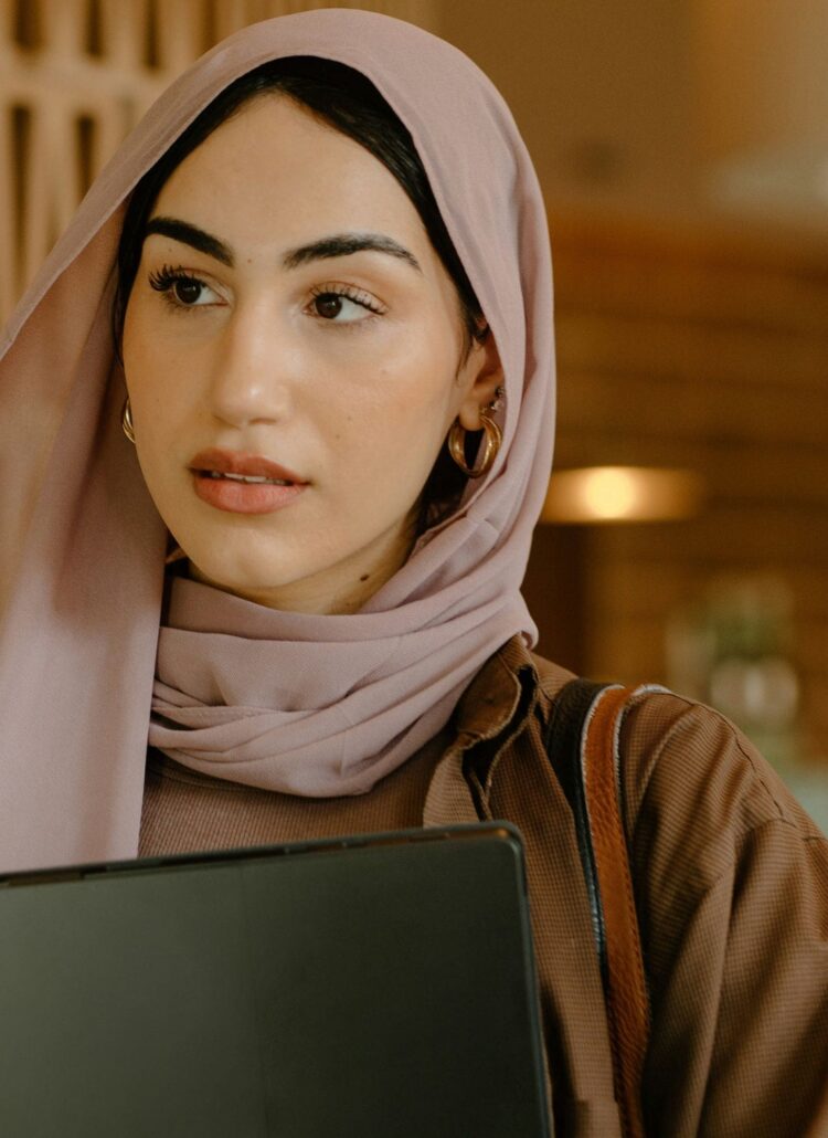 A woman in hijab holding a laptop, focusing on ways to silence your inner critic.