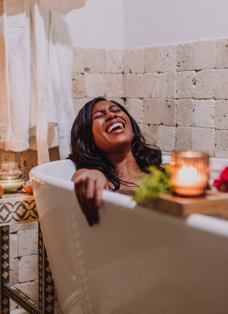 A woman enjoying a self care day, laughing joyfully while relaxing in a bathtub.