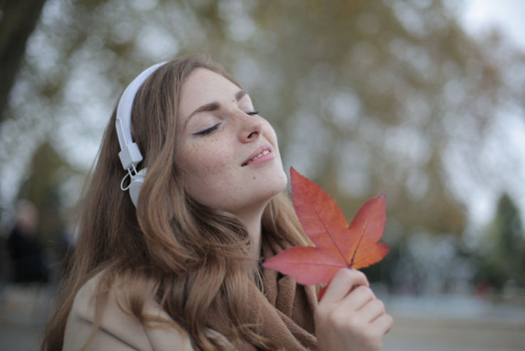 A woman with headphones enjoying the simple pleasure in life of holding a leaf.
